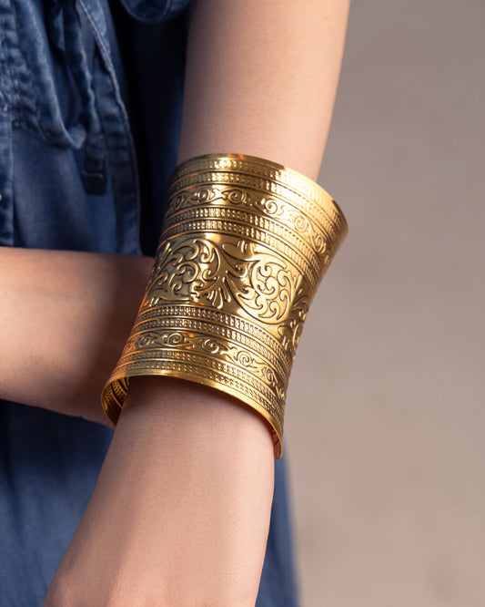 Gold bracelet with intricate designs on a person's wrist against a neutral background